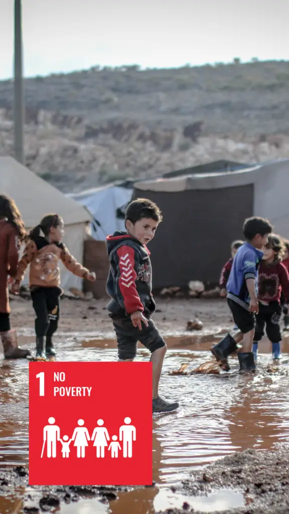 Refugee children inside a tent camp flooded with water, SDG 1 with red background that says "No Poverty" is in the left lower corner.