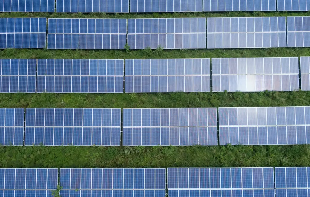 Aerial view of a solar farm with multiple rows of solar panels neatly arranged on a grassy field. net zero pathways