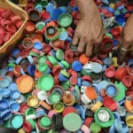 Various colored plastic lids spread out on the ground, with two hands sorting through them, suggesting an activity related to recycling or repurposing. Plastic Pollution Management