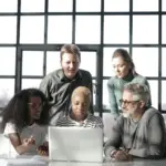 A diverse group of five individuals gathered around a laptop in a modern office, engaged in a collaborative task or discussion. Enhancing Knowledge for Mitigation and Adaptation