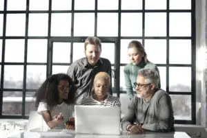 A diverse group of five individuals gathered around a laptop in a modern office, engaged in a collaborative task or discussion. Enhancing Knowledge for Mitigation and Adaptation