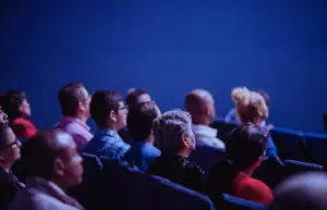 Audience in a theater or auditorium, facing towards a stage or screen, under dim lighting. Arab Forum for Environment